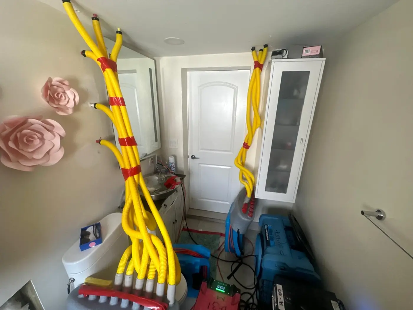 Yellow drying hoses feeding air into the lower wall of a water-damaged room